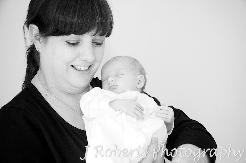 Mother smiling down at newborn baby in her arms - baby portrait photography sydney